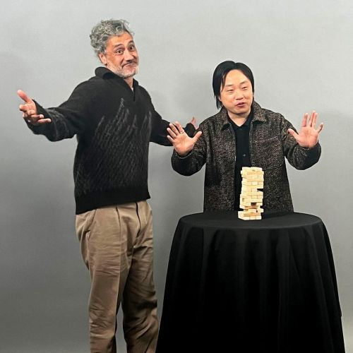 Taika waititi and Jimmy o Yang are playing jenga and throw their hands out impressed it didnt fall