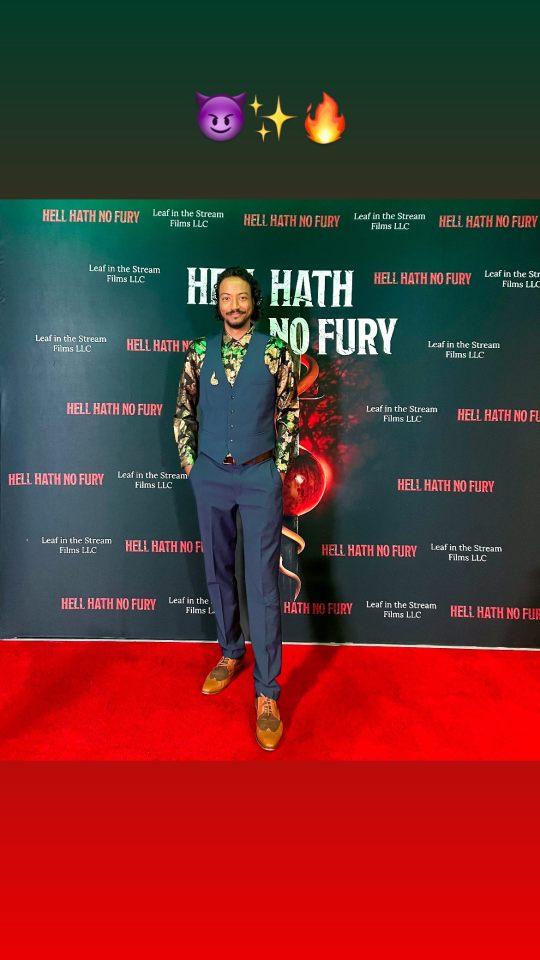 Picture of Samba schutte in a blue suit best with colourful undershirt sleeves standing in front of “Hell Hath No Fury” backdrop for the premiere.