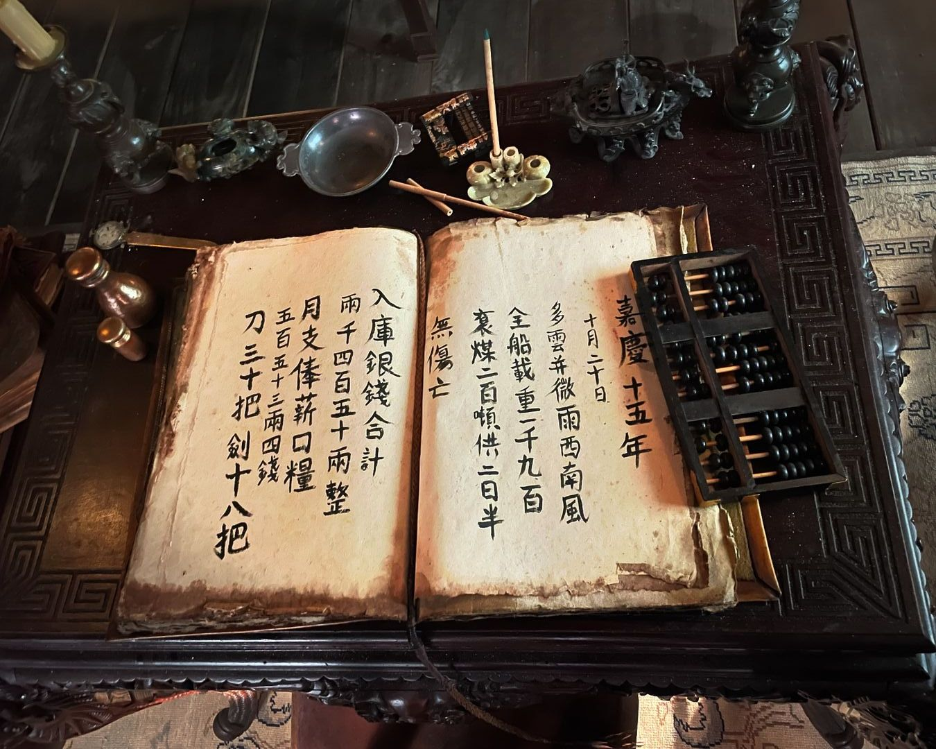 BtS picture of Zheng's office, an ornate table with Chinese written on aging paper, an abacus and other office stuff