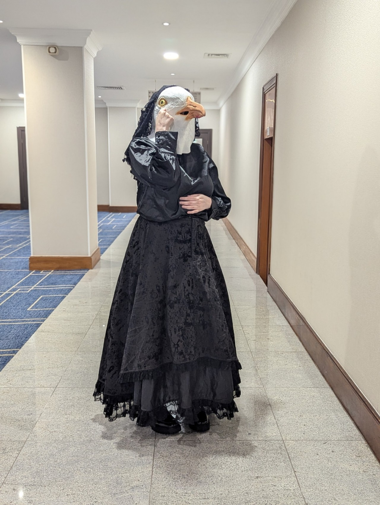 Picture of a woman in a black mourning dress with a seagull head dabbing her eye, and a veil. 