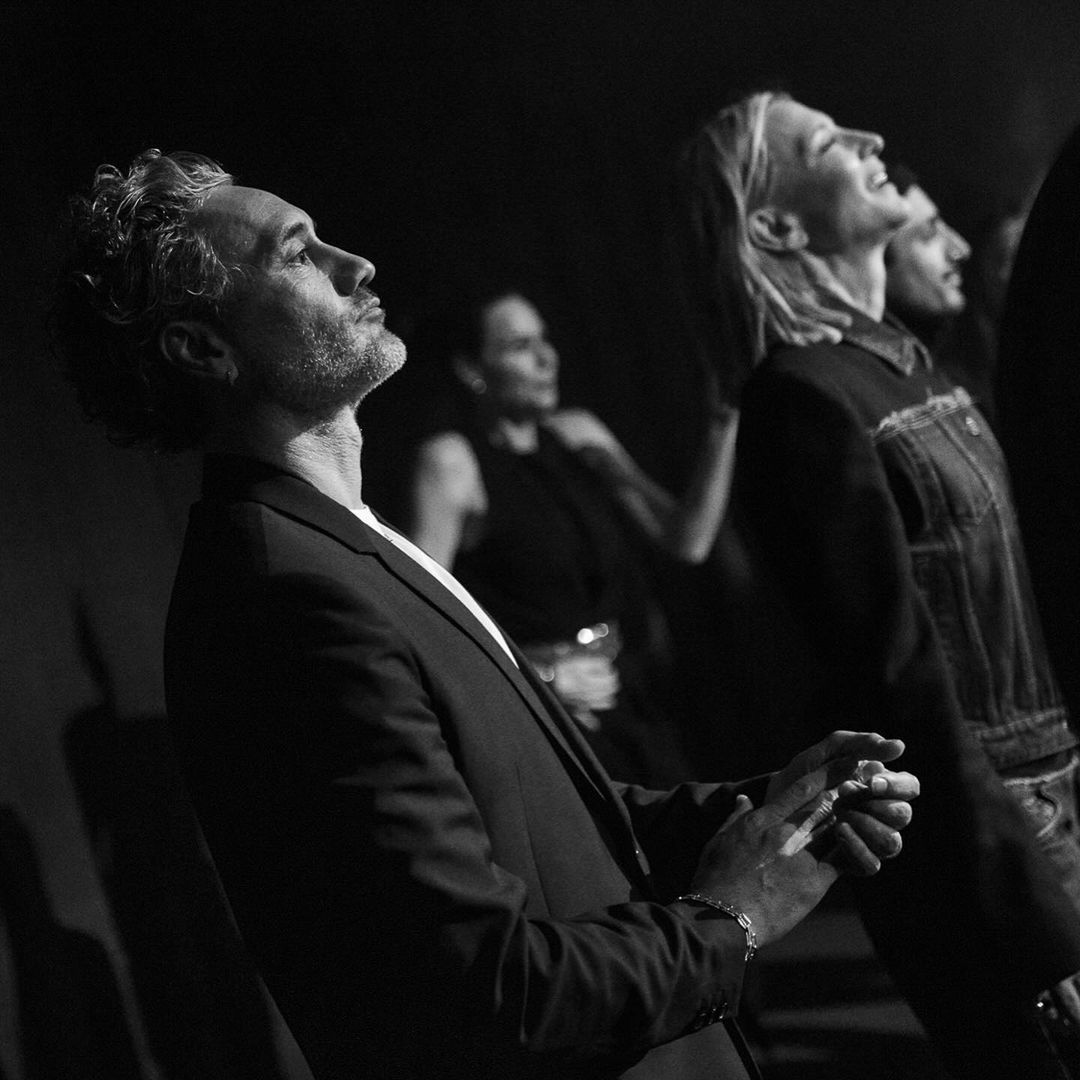 Black and white side profile picture of taika waititi in a suit standing next to cate blanchett