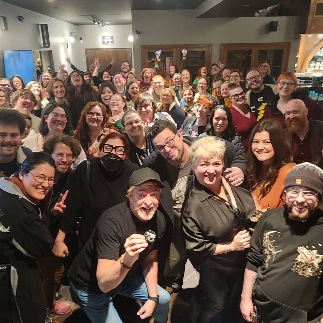 Photo of Rhys posing with a big group of fans after the Atlanta show, all of them smiling at the camera. Rhys is holding up what looks like a badge and some of the fans are holding up their hands in a peace gesture.