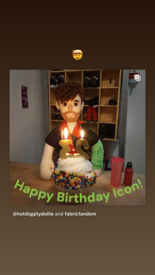 Insta story where Nathan shared a post from @ HotDiggityDollie AKA FabricFandom, above which he has added the 'mind blown' emoji. The original post is a photo of a homemade doll made to resemble Nathan's character from the show 'Newark, Newark', a man with brown hair and a short brown beard wearing a green cast, sitting in front of a cupcake decorated with sprinkles and candles in the shape of a 2 and a 3. 'Happy Birthday icon' is written in curving green letters at the bottom of the photo.