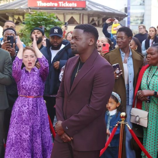 Daniel Kaluuya poses for cameras on a red carpet while Samson looks on from the crowd in the background.