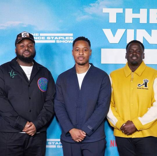 Samson, Daniel and director William Stefan Smith at the premiere of The Vince Staples Show. They are standing in front of a light blue background with the show's title on it and looking at the camera, each with their hands clasped in front of them. 