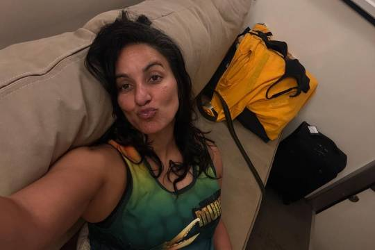 Selfie of Madeleine Sami on a narrow sofa or bench, her head leaning on the cushion behind her. She is wearing a green tank top and looking at the camera with an exaggerated duck face pout.