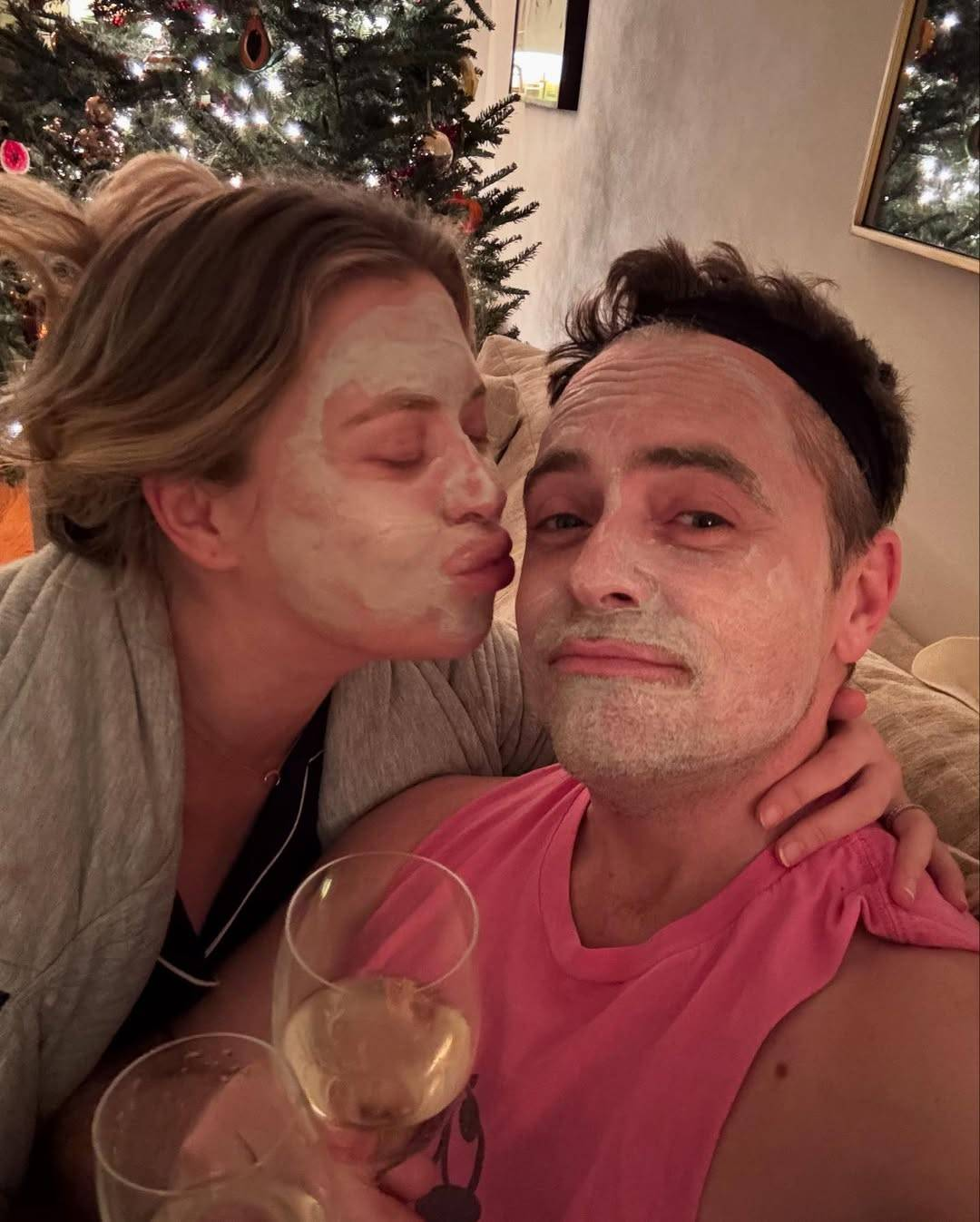 Selfie of David and his wife Kinga at home. They have both applied a facial mask and are holding a glass of white wine each. David is looking at the camera and Kinga is about to kiss him on the cheek, her lips pursed and her hand on the back of his neck.