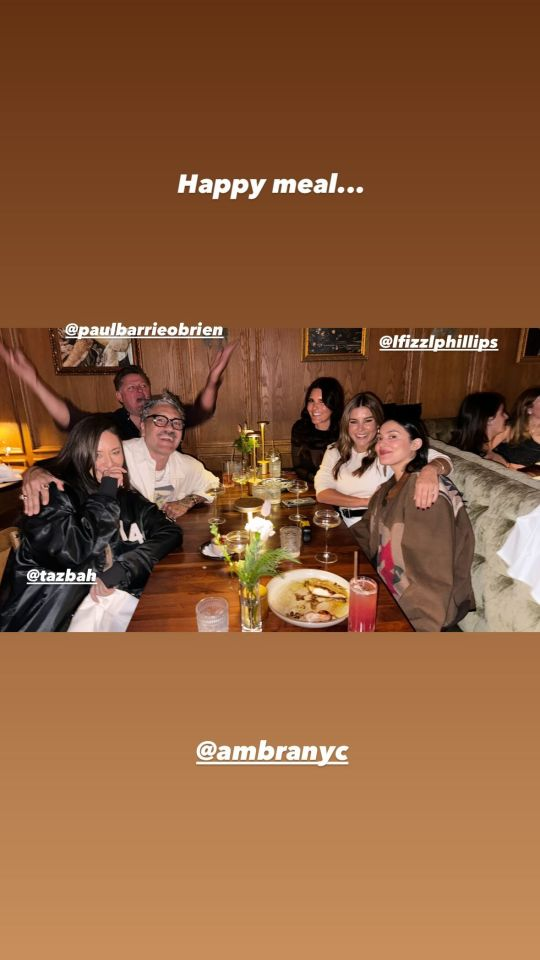 Instagram story with a photo of Taika and a group of friends sitting at a restaurant table with various drinks in front of them. They are all smiling or laughing and Taika has placed one arm around the shoulders of the woman sitting next to him. Text above reads ‘Happy meal …’ and he has tagged @ AmbraNYC as well as some of his friends: @ PaulBarrieOBrien, @ tazbah and @ lfizzlphillips.