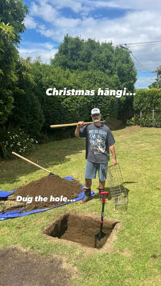 Photo of Taika in a backyard, a shovel on his shoulder and a metal basket in his other hand. He is standing in front of shallow rectangular pit in the ground. Text reads: 'Christmas hangi ... Dug the hole ...'