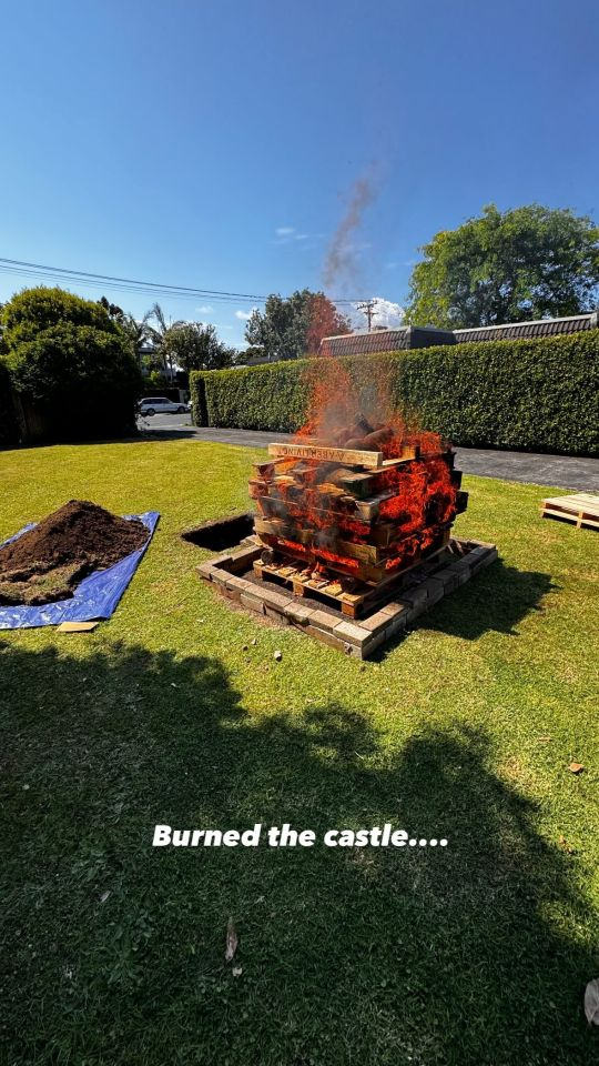 Photo of the stack of pallets, shot from another angle and further away. They are now on fire, heating the rocks at the top so they can be used to cook food inside the pit. Text at the bottom reads: 'Burned the castle ...'