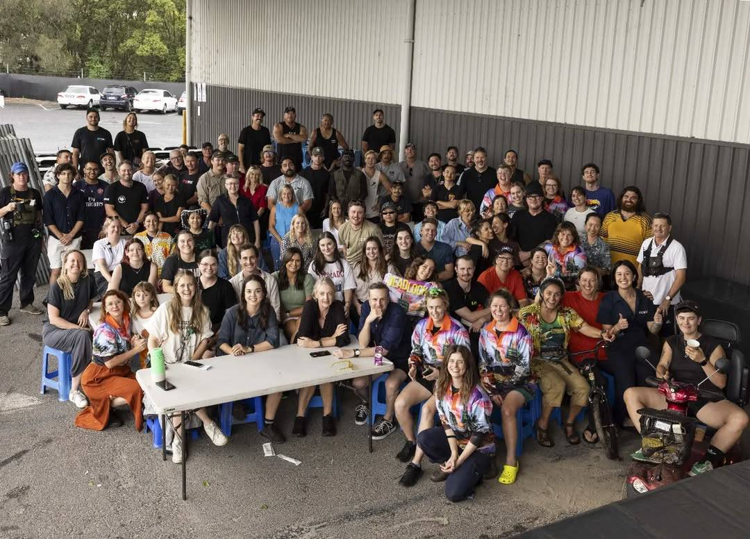 Group photo of the cast and crew of Deadloch season 2, taken from above in a paved lot, probably outside the studio where the season was filmed.