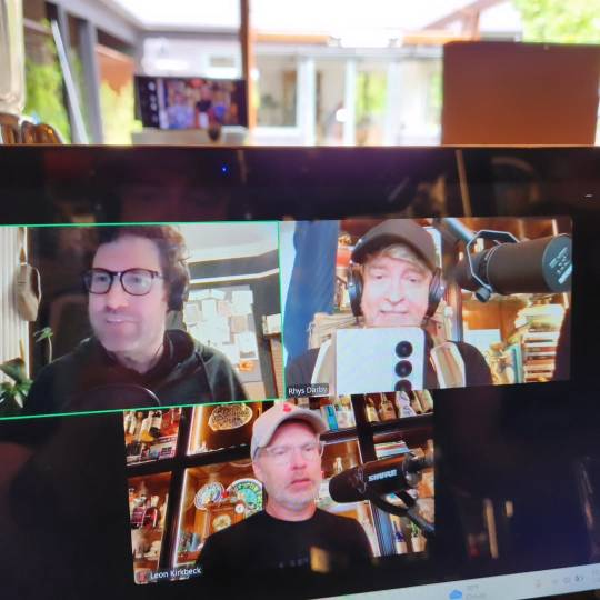 Photo of Rhys's laptop screen, which shows him and his podcast co-hosts, Buttons and Dan Schreiber, in a video call. Rhys is wearing the canvas backpack.