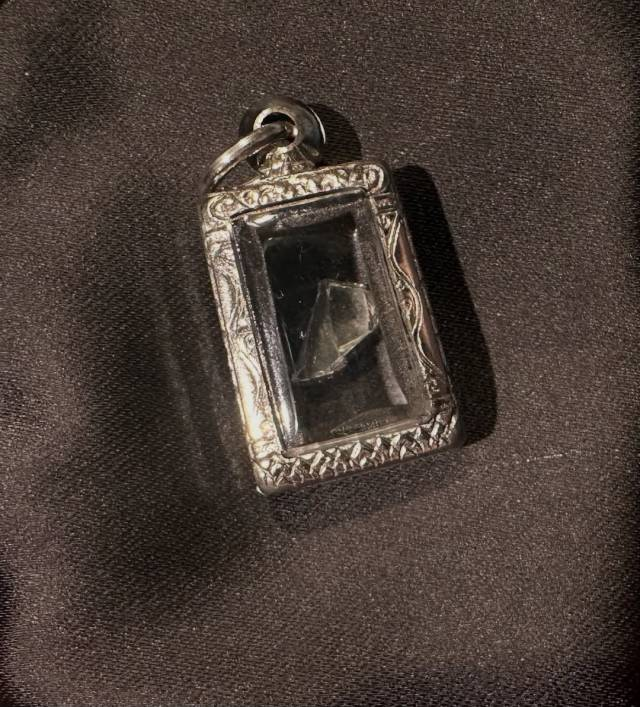 A rectangular locket with a silver frame and a clear center containing a small shard of clear glass.