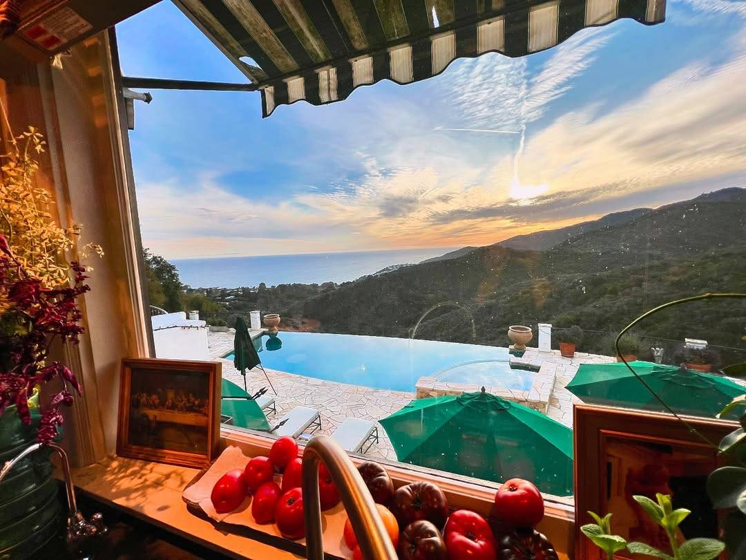 Another photo of the sunset seen through the same window, taken at a slightly different angle, with the camera pointed more towards the ocean and held up higher so the sun can be seen just above the hills.