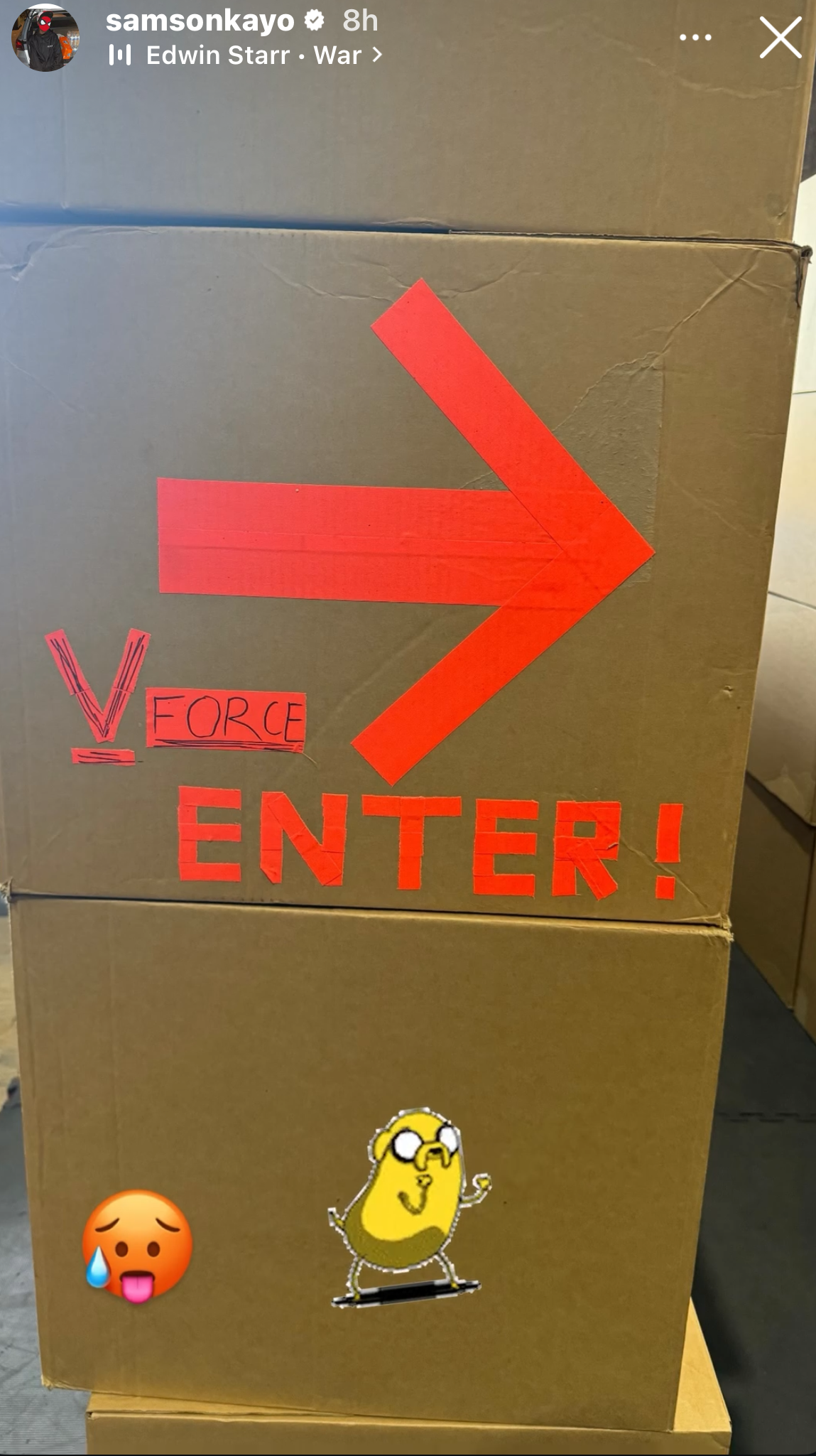 Another photo from Samson's Insta stories: 4 cardboard boxes stacked on top of each other, one of which features a bright red arrow and the words 'V Force, enter!' At the bottom of the photo, Samson has added a 'sweating with tongue hanging out' emoji and a (probably) animated image of Jake the Dog from Adventure Time either dancing or doing a boxing stance - hard to tell!