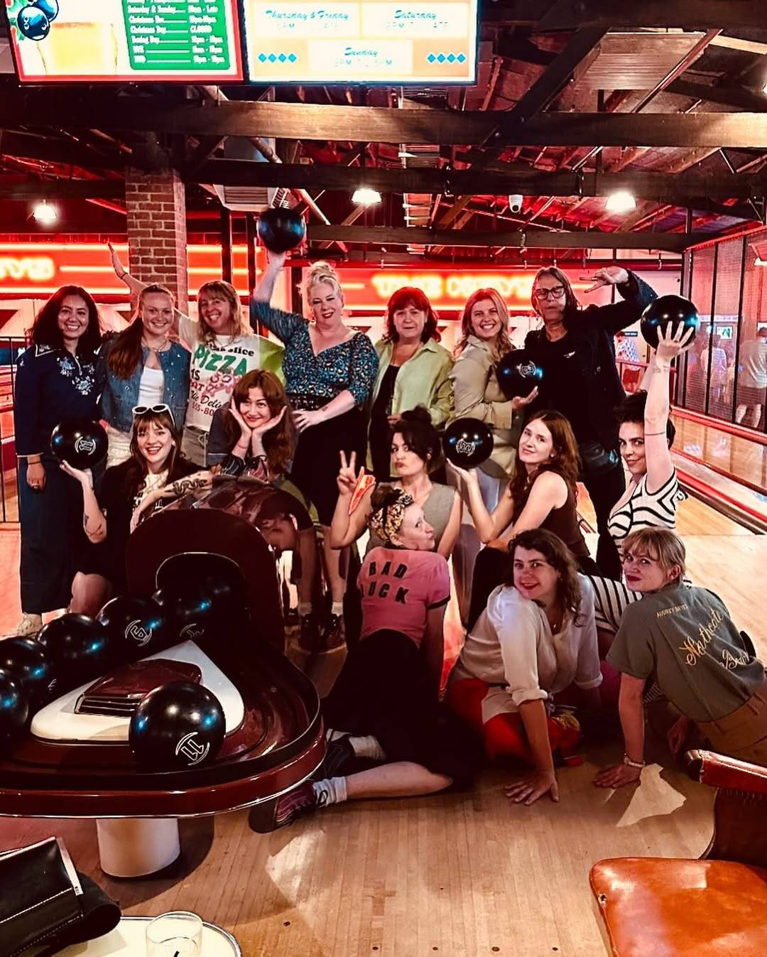 Group photo of the ‘All Her Fault’ costume design crew at a bowling alley. They are looking at the camera and striking various poses, some holding up their bowling balls.