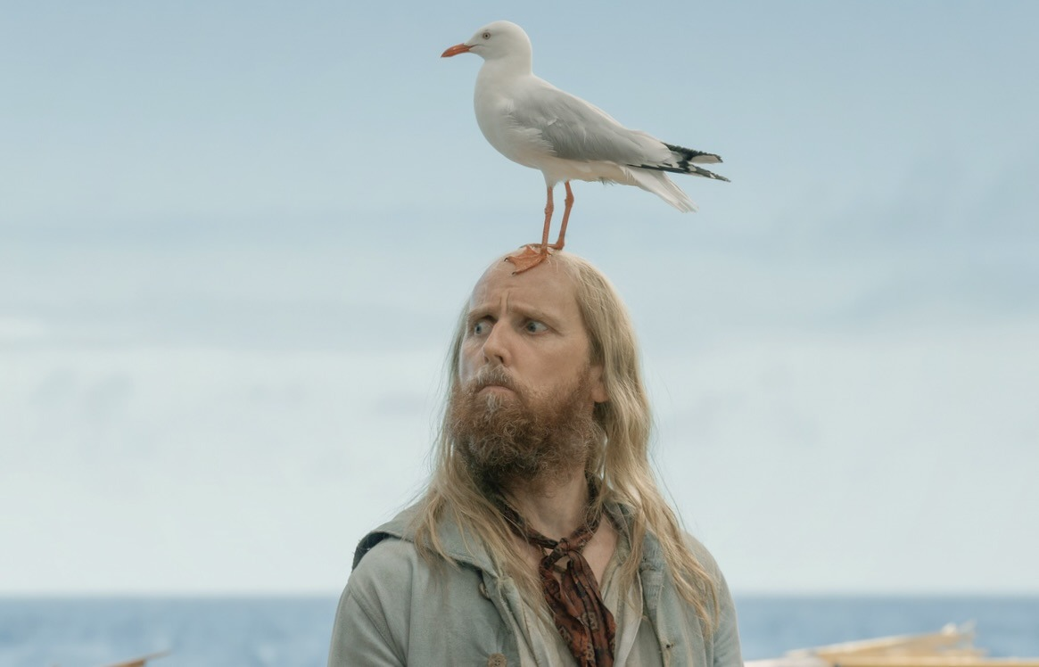 A production still from OFMD season 1: Ewen Bremner as Buttons looks off to the side with Karl the seagull sitting on his head.