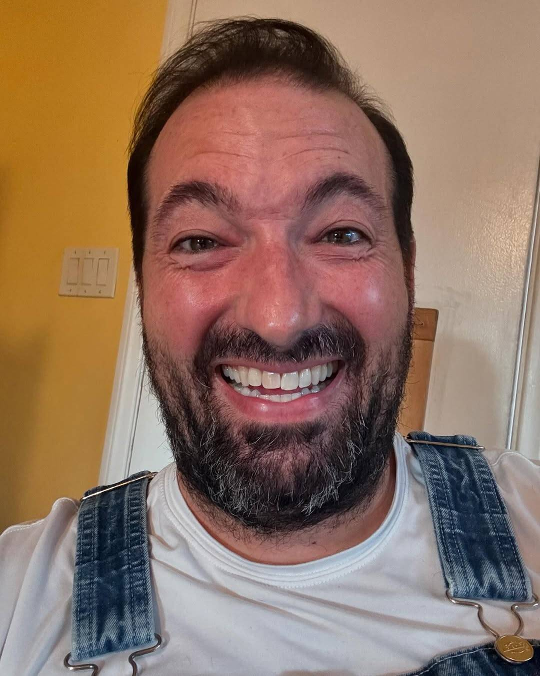 Selfie of Christopher Corbin, who is looking at the camera with a big open-mouthed grin bordering on creepy (the caption on his Instagram post describes it as 'an overly forced smile'). His previously long black hair and beard are both trimmed much shorter now.