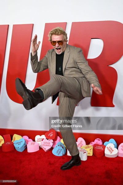 Another red carpet photo of Rhys. This one is shot slightly from the side and Rhys is facing away while doing some kind of martial arts kick, his mouth wide open as if in a shout.