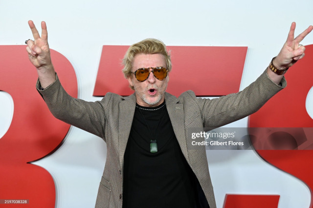 Another closer-up red carpet photo. Rhys is shown from about the hips up with both hands in the air and making peace signs. He is looking directly at the camera with his mouth open in an O shape.