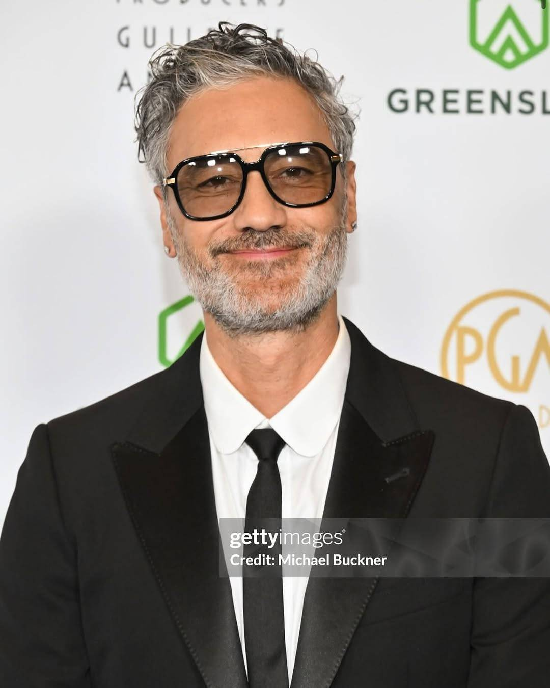 Getty Images photo of Taika at the PGA Awards show, shown from the chest up. He is looking directly at the camera with a big closed-mouth smile.