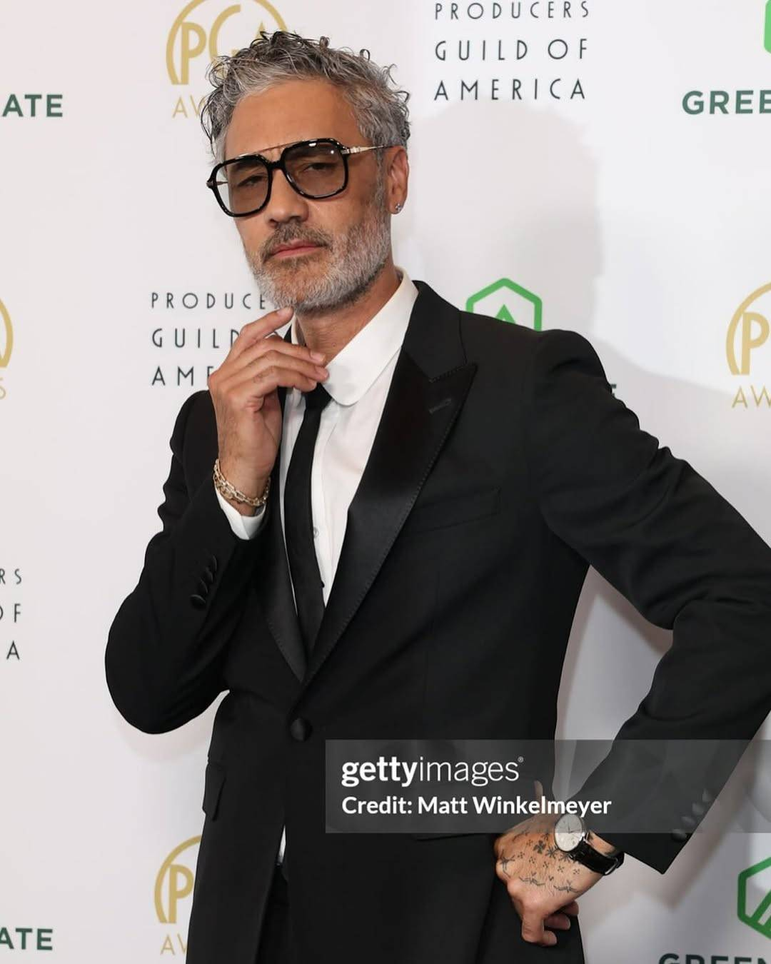 Another Getty Images photo of Taika. This one shows him from the hip up, slightly turned away to pose dramatically with one hand on his hip and the other raised to just below his chin. Taika is looking at the camera with a mock-thoughtful expression, eyes narrowed and forehead creased in a frown.