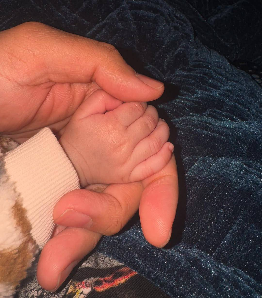 Photo of a baby’s tiny forearm and hand, held very gently in one of Guz’s hands.