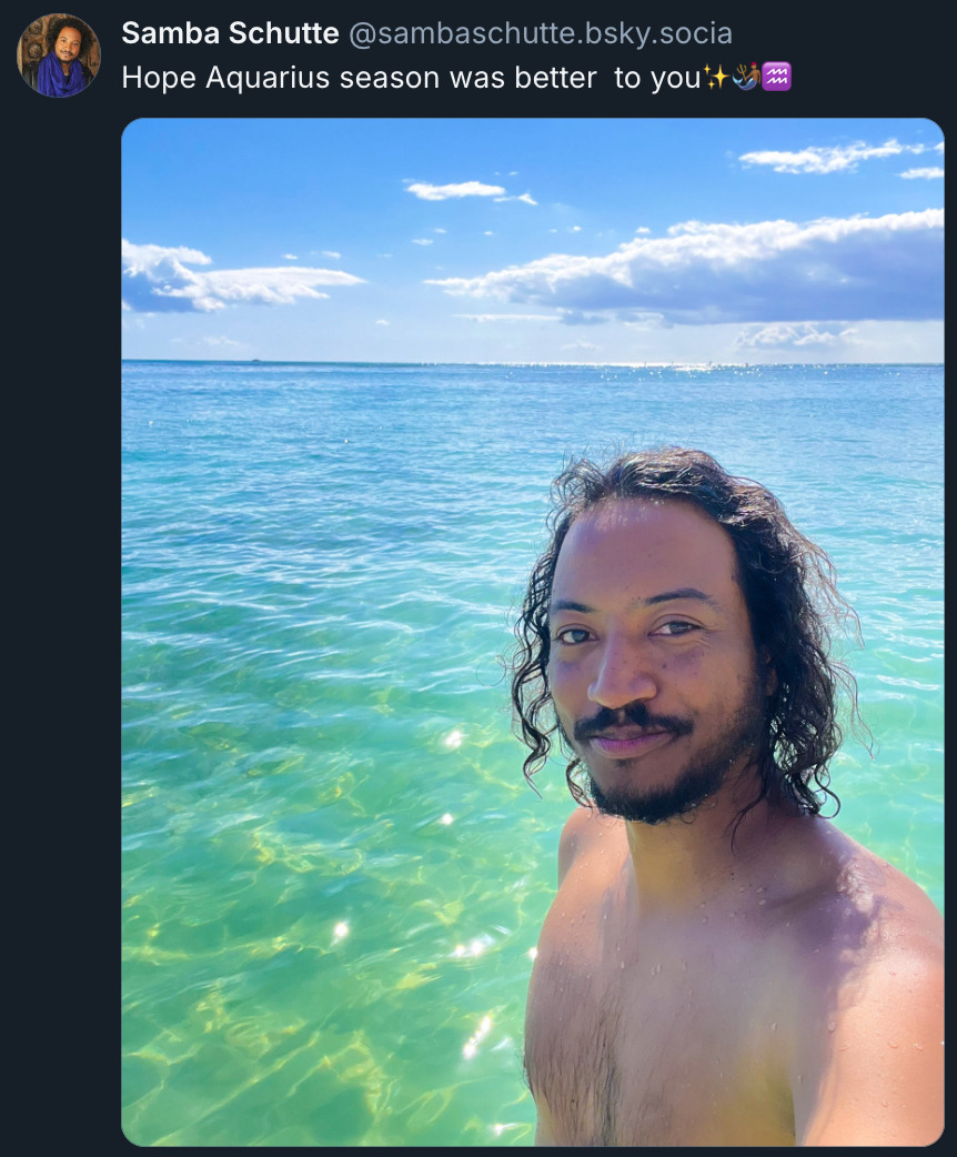 Bluesky post by @ SambaSchutte.bsky.social‬ with a selfie of Samba smiling as he stands in shallow water on a sunny day, and the text: 'Hope Aquarius season was better  to you (3 emojis: Sparkles, Merman, Aquarius Zodiac Symbol).'