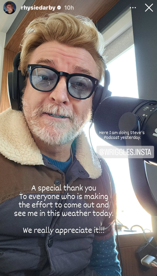 Instagram Story from @ RhysieDarby: a selfie of Rhys sitting in front of a microphone, wearing a pair of headphones, blue tinted glasses and a leather jacket with a sheepskin collar. He is looking down at the camera with his eyebrows raised and lips parted. He has tagged wriggles.insta and added the following text in a white Comic Sans-like font: ‘Here I am doing Steve's podcast yesterday. A special thank you to everyone who is making the effort to come out and see me in this weather today. We really appreciate it!!!’