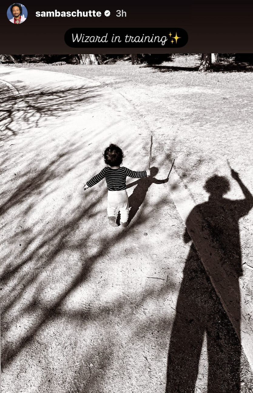 Samba's Instagram Story with a black & white photo of his kid seen from behind, holding a stick in one hand like a wand. Behind them, Samba's own shadow can be seen also holding up a stick. Above the photo, Samba has added in cursive font: 'Wizard in training (sparkle emoji)'.