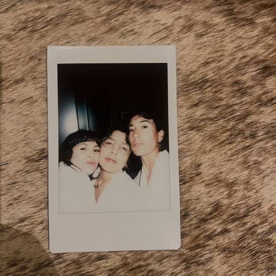 Photo of a polaroid showing Vico and their partners standing close with their faces pressed together. They are seen from the chest up, all 3 of them dressed in white.